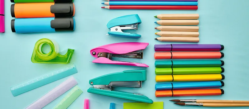 Staplers, markers and pencils arranged on a teal background