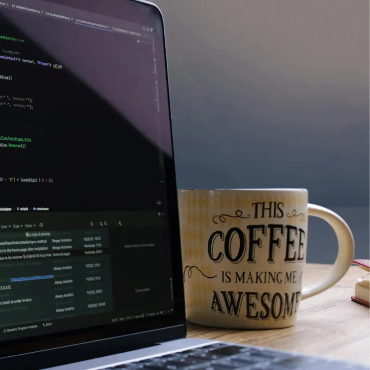 Laptop with code on screen beside a coffee mug