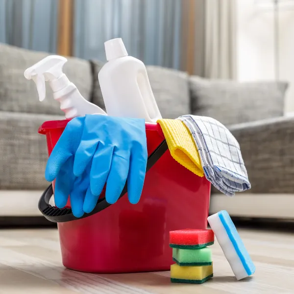 Red bucket filled with cleaning sprays, sponges and gloves