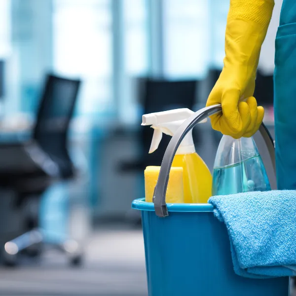 Gloved hand holding a bucket of cleaning supplies in a modern office