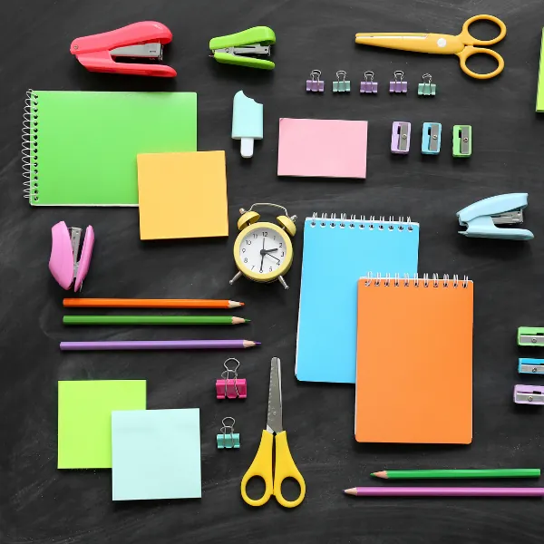 Colourful office stationery including sticky notes, scissors and pens arranged on a dark desk